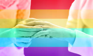 people, homosexuality, same-sex marriage and love concept - close up of happy lesbian couple hands putting on wedding ring over rainbow flag stripes background
