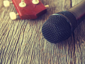 a black microphone and an ukulele on a wooden background representing a dj and a band.