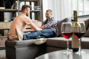 A gay couple sitting on the couch having open conversations about marriage with glasses of wine.