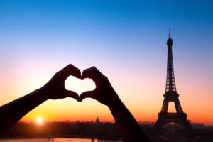 Couple in Paris making a hand heart while considering honeymoon destinations