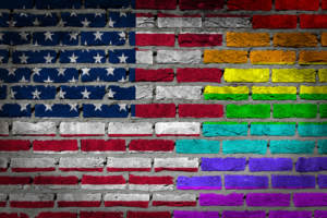 An American flag on a brick wall with LGBTQ stripes