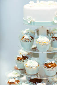 A wedding cake with a variety of cupcakes tiered below it