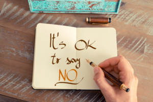 A person writing It's "OK to say NO" in a journal,