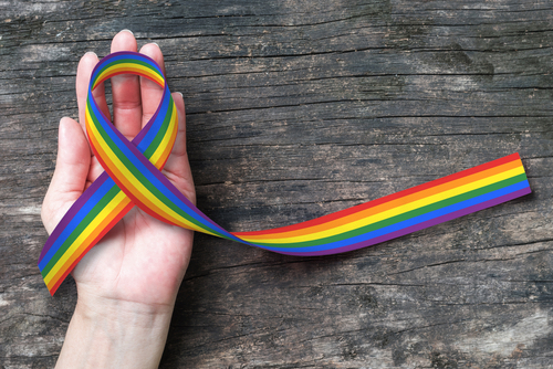 A hand holding a rainbow ribbon to connect to LGBT history.
