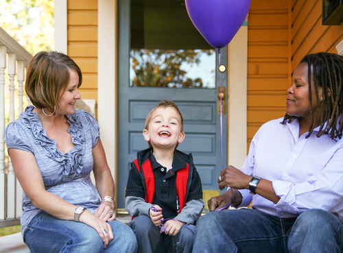 A same-sex couple sitting on a porch with their child addressing starting families