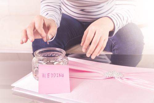 A person putting a coin into a jar to help save for their wedding.