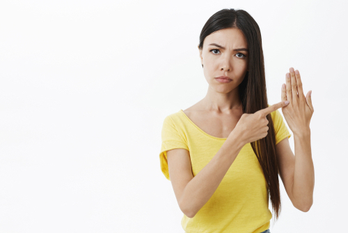 Asian woman pointing to her bare ring finger safely dropping hints about marriage.