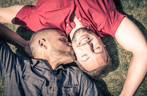 A same-sex couple lying in the grass taking the first steps after their engagement