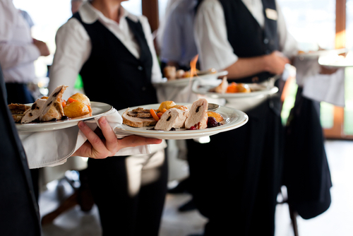 Vendors carrying plates with meat dish at a wedding