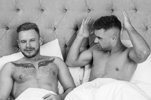 Gay couple in bed having a disagreement and considering a sleep divorce.