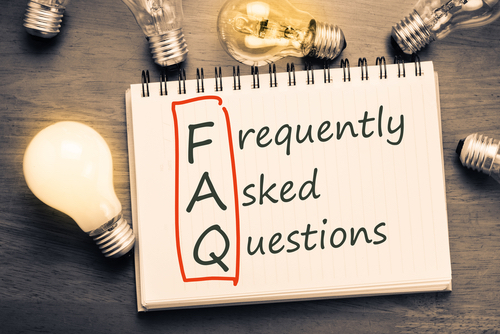 Notebook with Frequently Asked Questions written on it and FAQ outlined surrounded by light bulbs. 