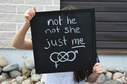 A non-binary person holding a sign that says not he not she just me 