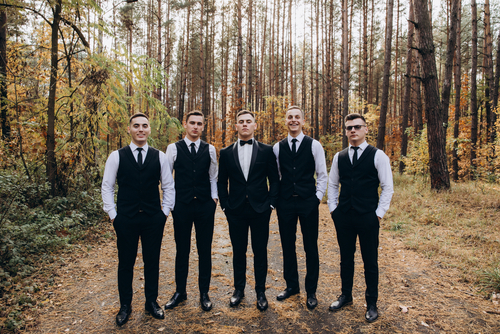Groom and his groomsmen standing in a forest during autumn for a wedding