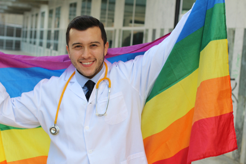 A smiling doctor holding a rainbow flag represents why you should come out to your healthcare provider
