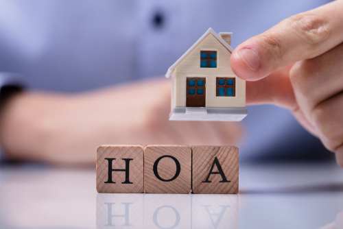 Wood blocks spelling HOA and a small house model being held representing homeowners’ associations