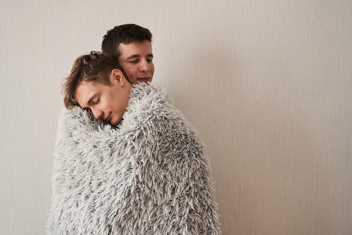 Gay couple embracing wrapped in a blanket