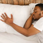 man sleeping alone with his hand on the pillow next to him