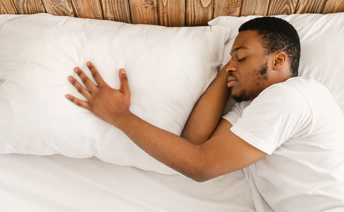 man sleeping alone with his hand on the pillow next to him