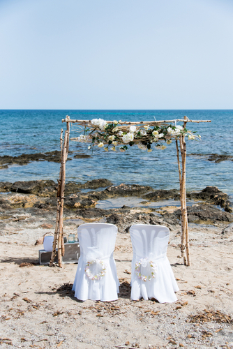 Two chairs on a beach with a marital arch used for planning an intimate wedding.