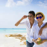 Gay couple together on a beach drinking from a coconut