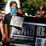 BLM protestors carry a sign referencing the arc of the moral universe