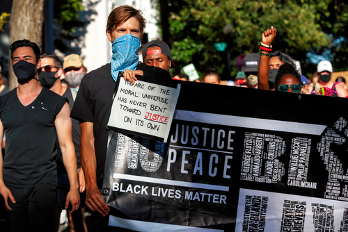 BLM protestors carry a sign referencing the arc of the moral universe