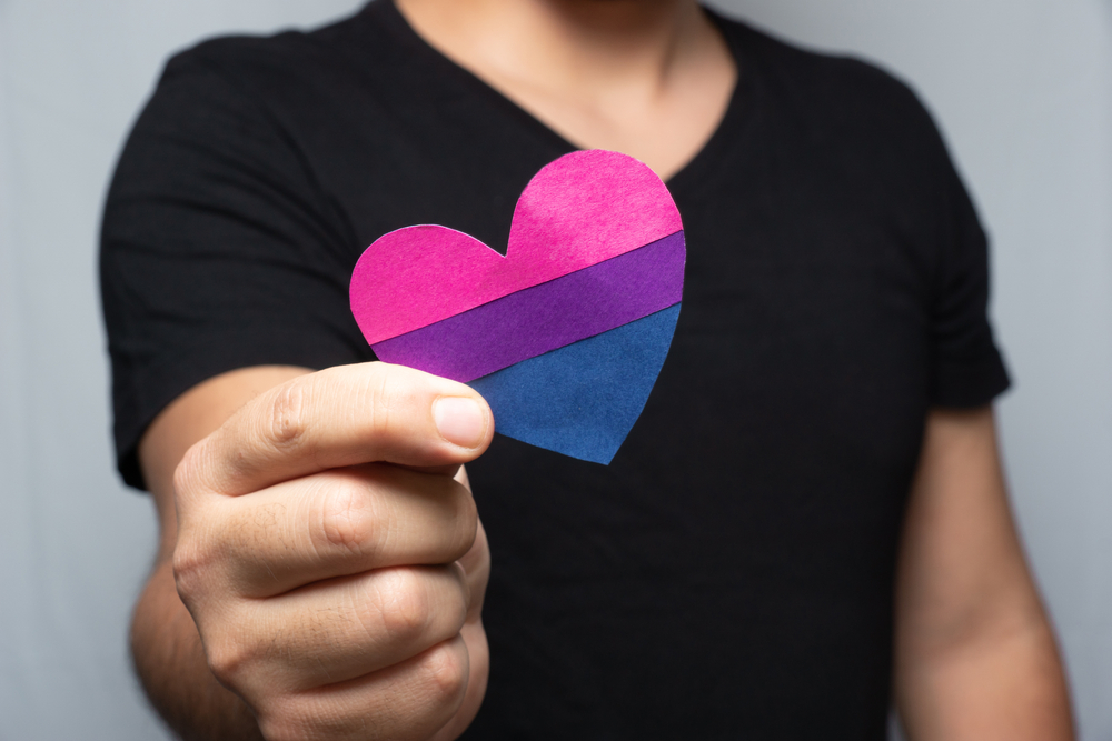non-monosexual person holding a bisexual flag paper heart