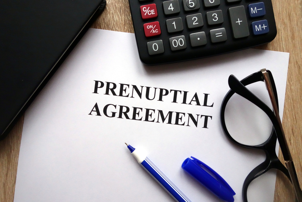 Prenuptial agreement printed on paper sitting on a desk with a pen and glasses preparing to write prenups