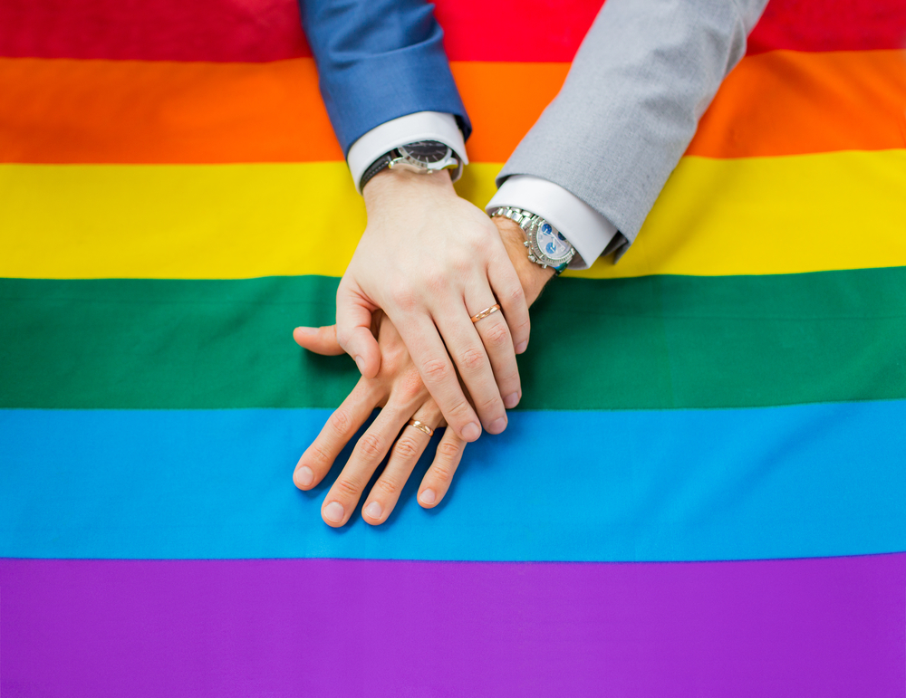 Gay married couple holding hands over a rainbow flag incorporating pride into their wedding.