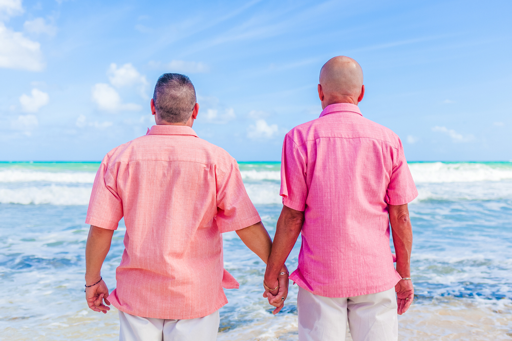 Same-sex couple holding hands on the beach of one of the best honeymoon destinations