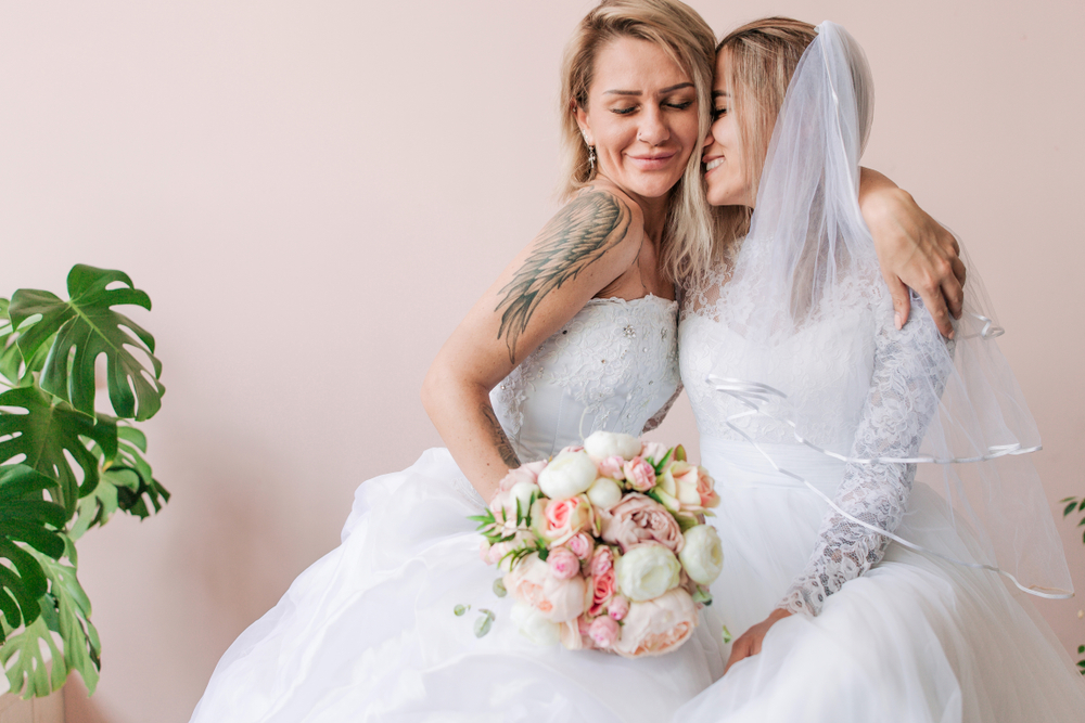 a same-sex couple embracing in wedding gowns thanks to advice that helped them plan their wedding.